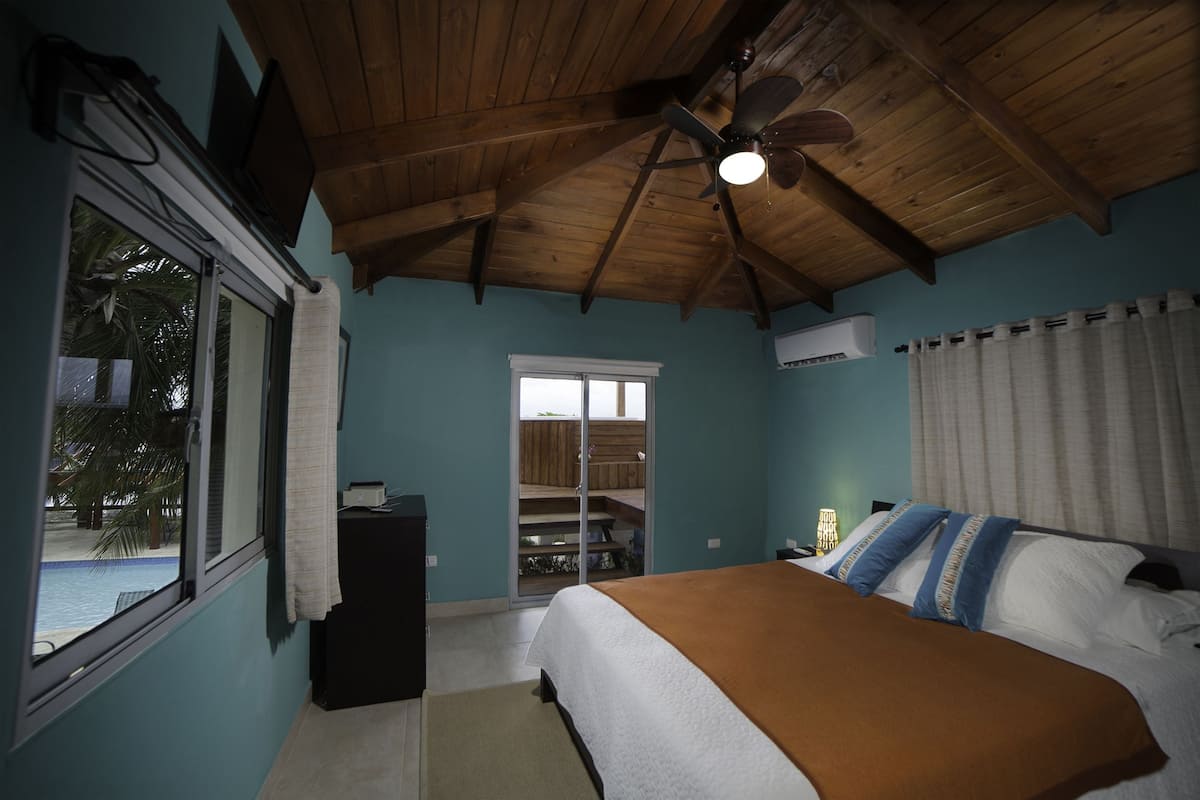 A bedroom with a bed, a ceiling fan, a window, and a view of a pool.