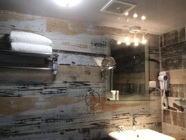 Un baño con pared de madera rústica, un espejo, un perchero para toallas, un lavabo y un secador de pelo.