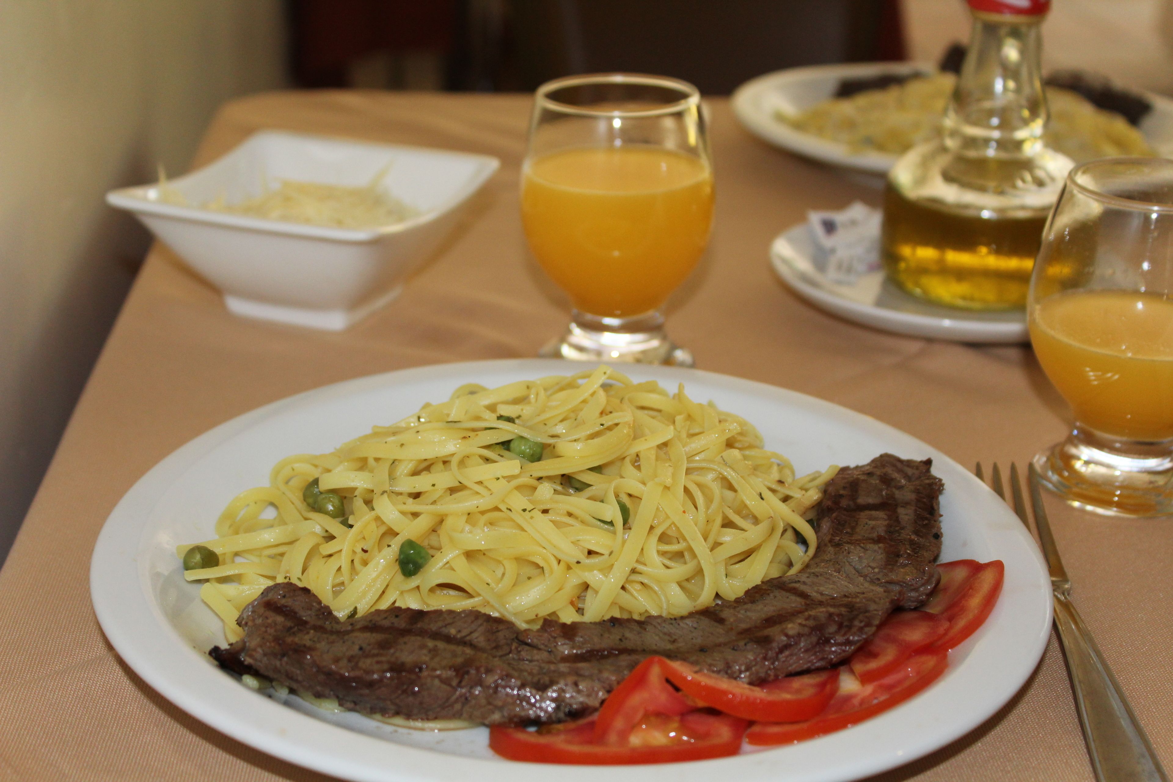 Un plato de espagueti con carne y tomates, un vaso de jugo de naranja y una botella de aceite de oliva sobre una mesa.