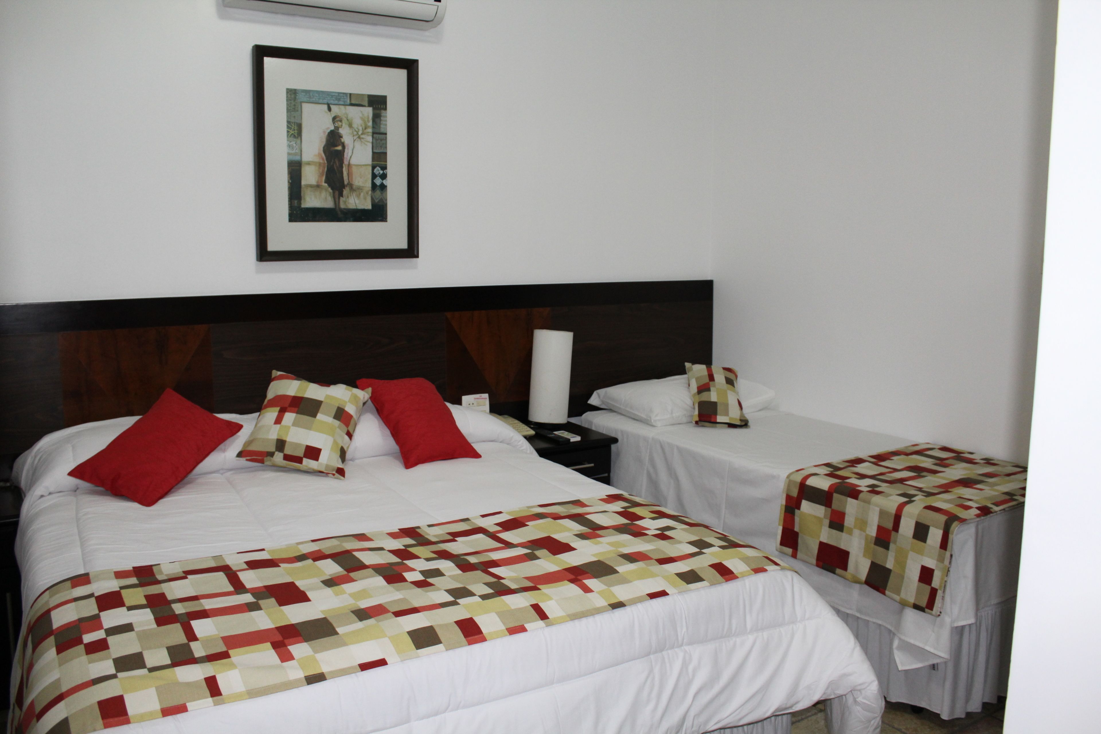 A hotel room with two beds, each with a quilted bedspread and pillows. There is a framed picture on the wall above the beds.