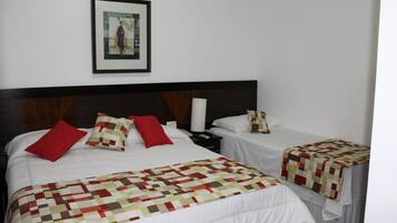A hotel room with two beds, each with a quilted bedspread and pillows. There is a framed picture on the wall above the beds.