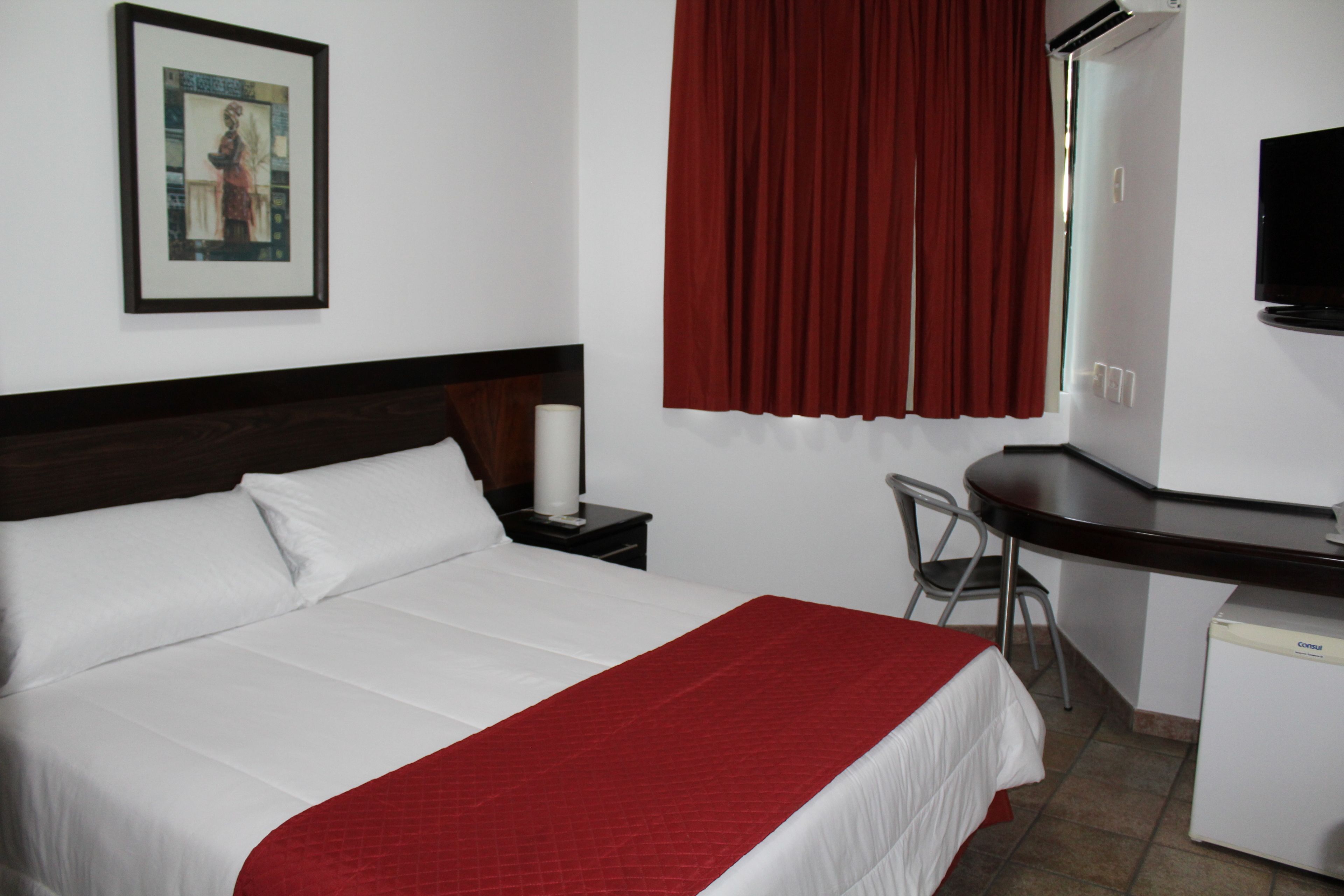 Ein Hotelzimmer mit Bett, Schreibtisch, Stuhl, Fernseher und einem Fenster mit Vorhängen.