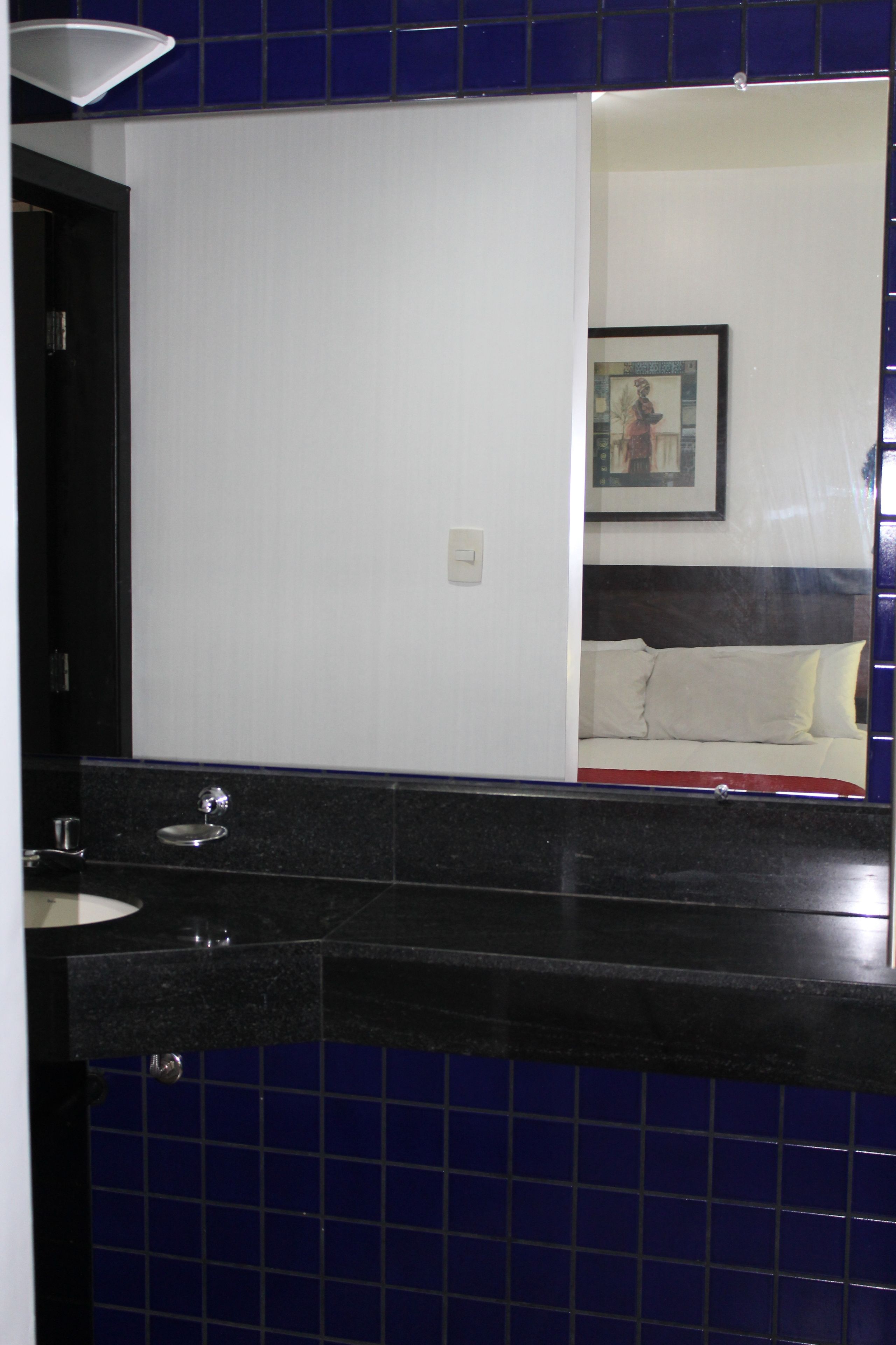 Un baño con espejo, lavamanos e inodoro. Hay un cuadro en la pared.