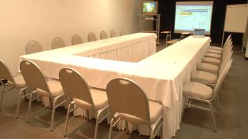Un salón de conferencias con una larga mesa, sillas, un proyector y una pantalla.
