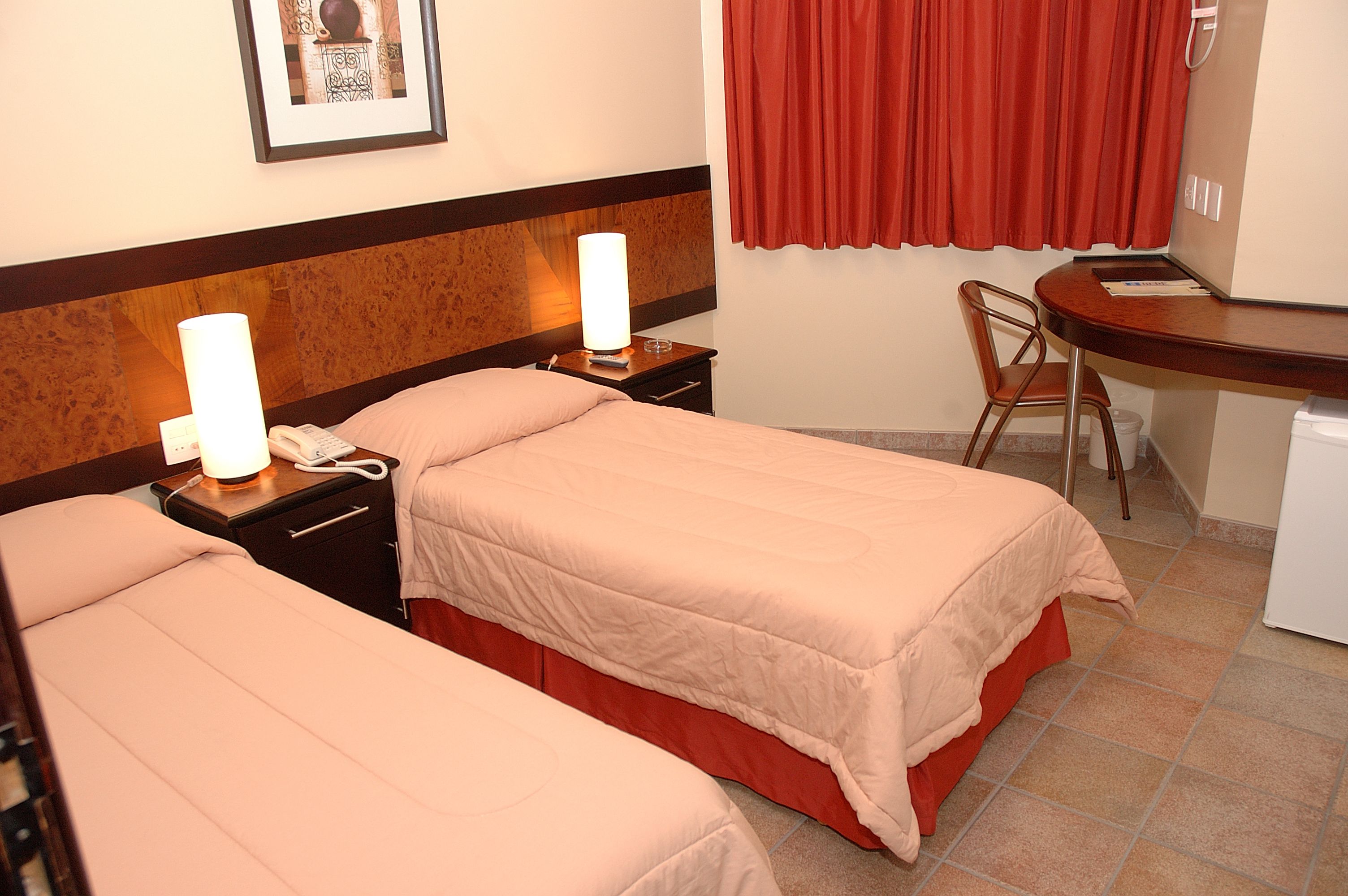 A hotel room with two beds, a desk, a chair, and a small refrigerator.