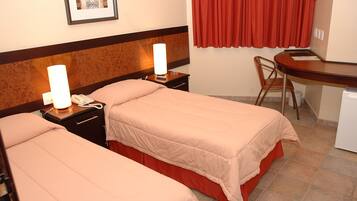 A hotel room with two beds, a desk, a chair, and a small refrigerator.