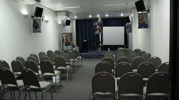Ett konferensrum med rader av stolar, en scen med en blå bakgrund och en vit projektionsduk.