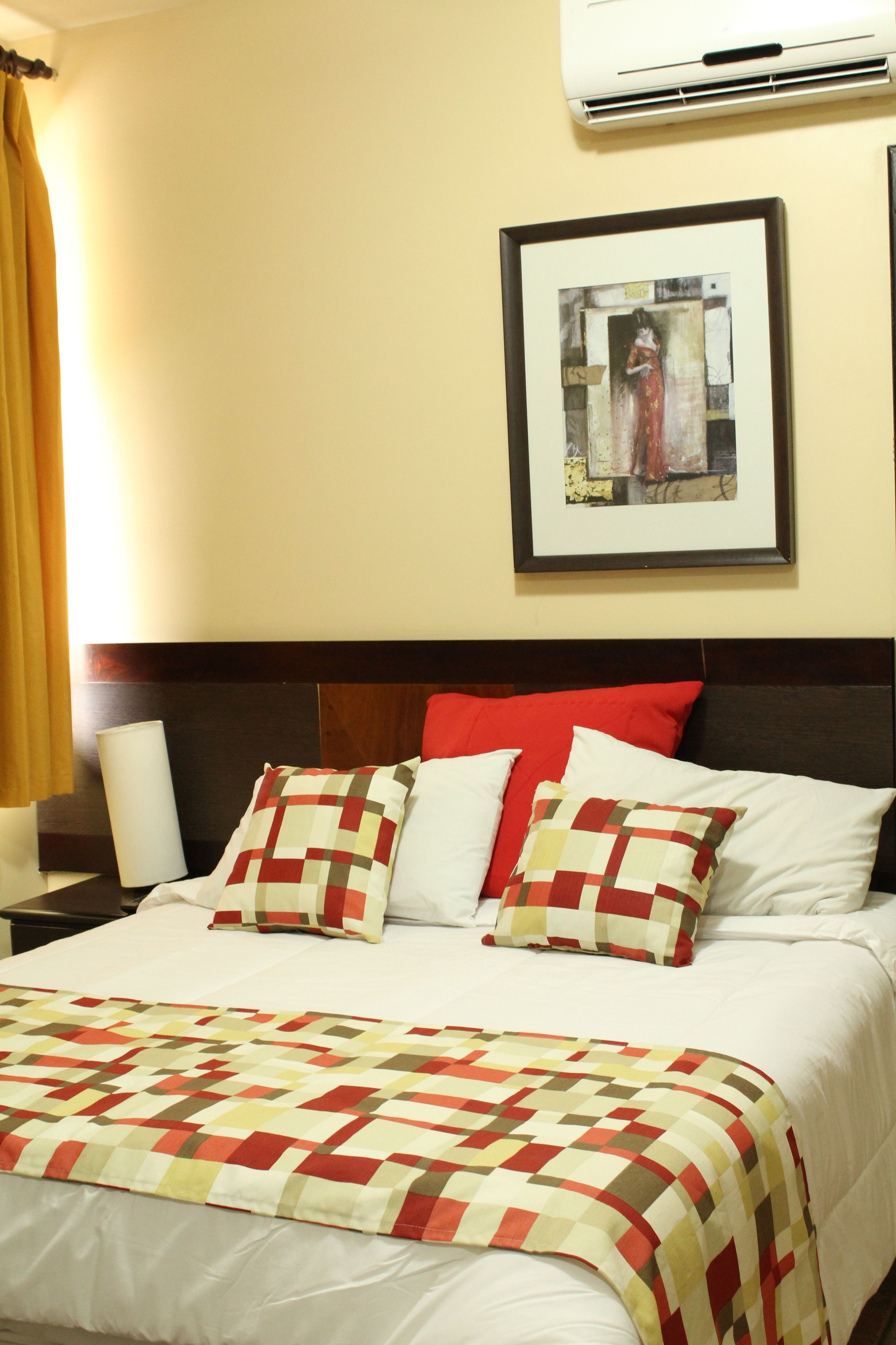 A hotel room with a bed, a framed picture on the wall, and an air conditioner above the bed.