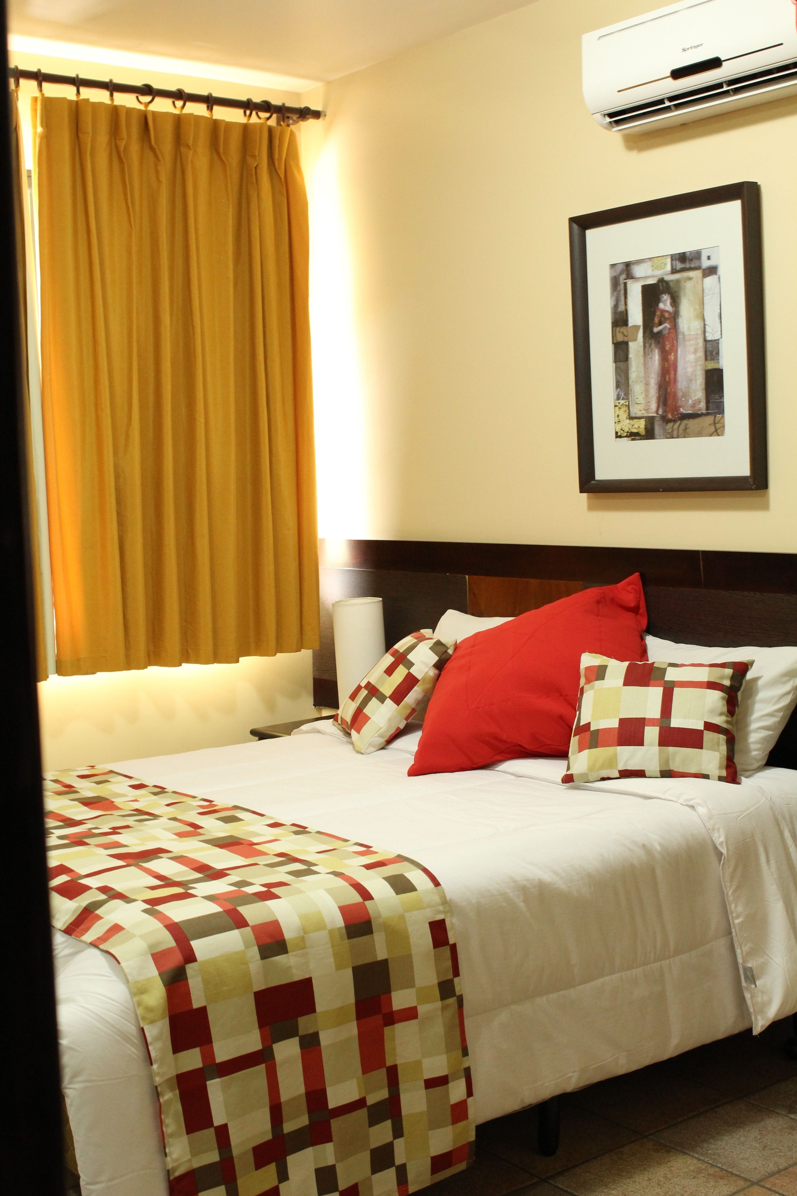 Quarto de hotel com cama, janela com cortinas, ar condicionado fixado na parede e quadro emoldurado.