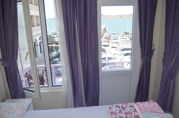 Una habitación con cama, una ventana con cortinas moradas y vistas a un estacionamiento y al agua.