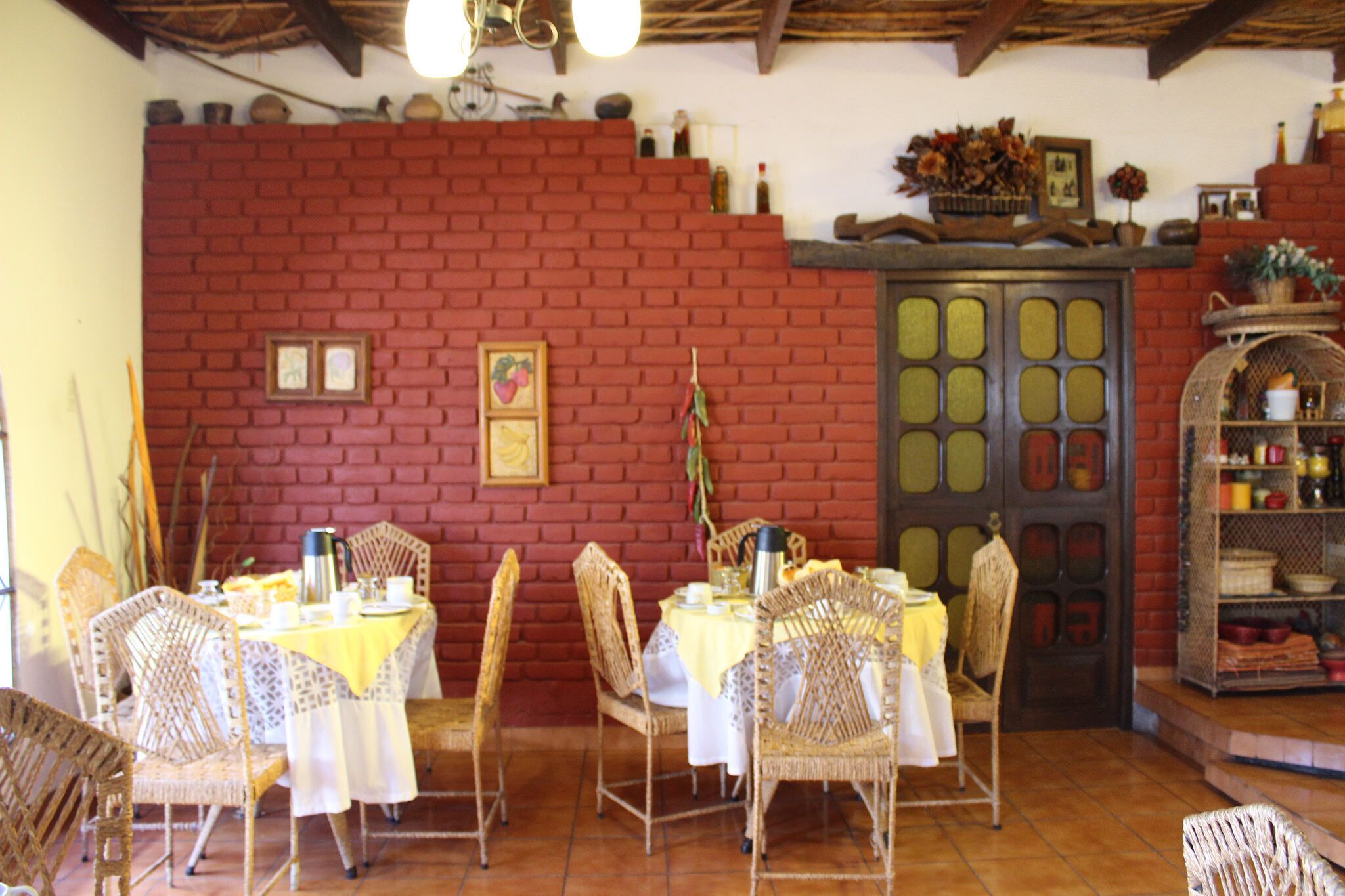 A dining area with wicker chairs and a table set for four, a brick wall, and a shelf with various items.