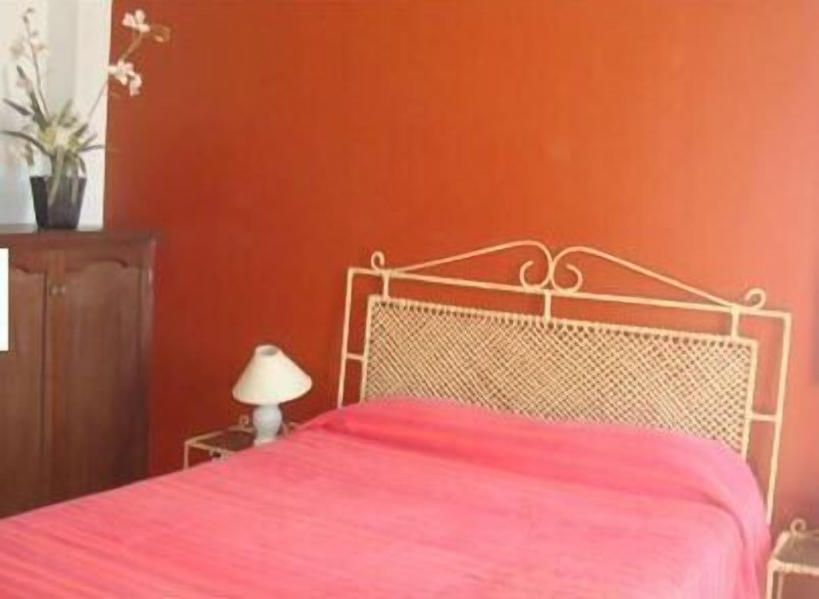 A room with a bed, a nightstand, a lamp, and a potted plant.