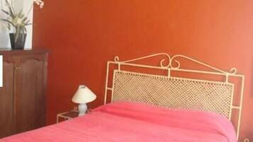 A room with a bed, a nightstand, a lamp, and a potted plant.