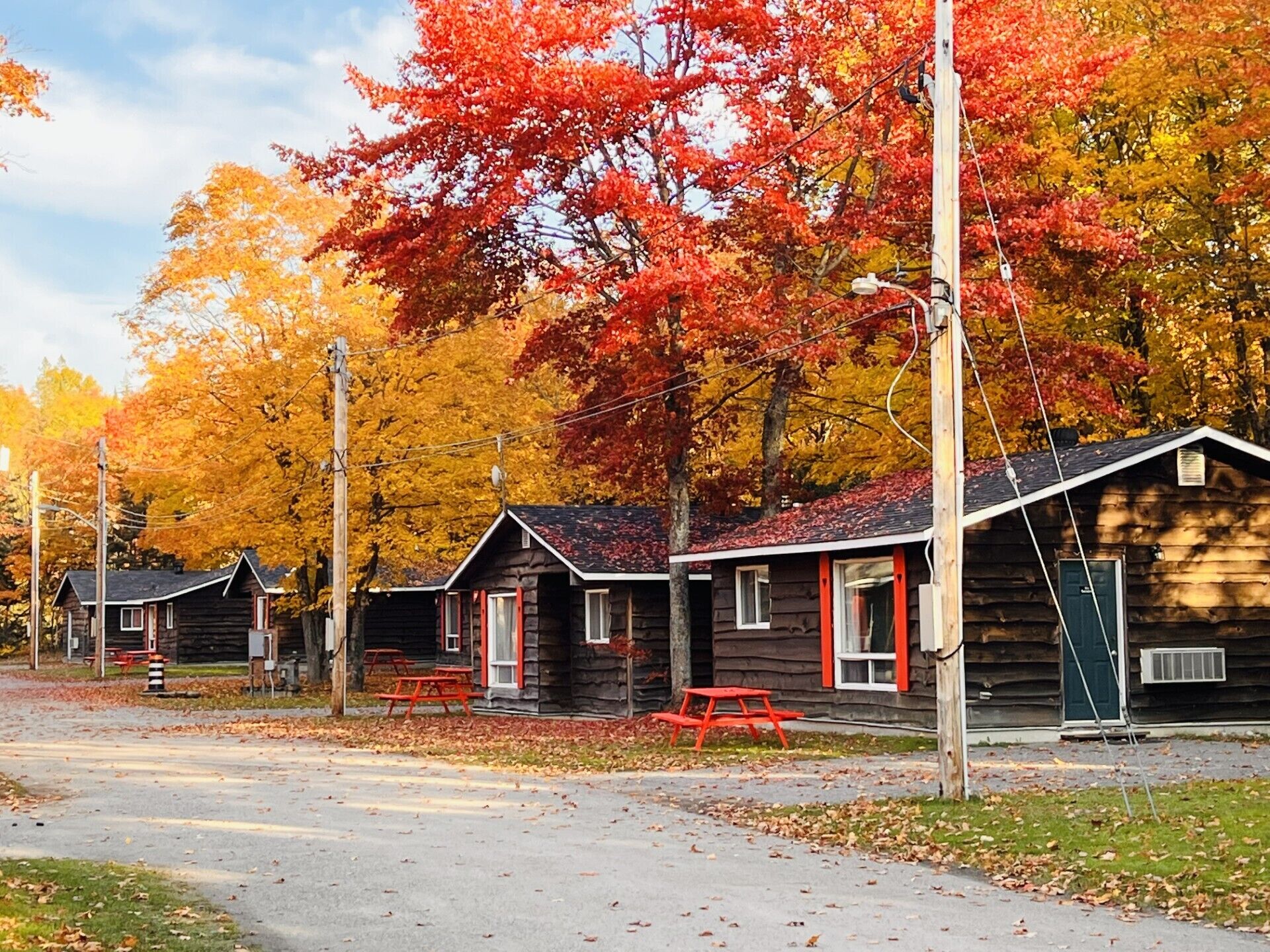 A row of log cabins with red trim, picnic tables, and a clear sky.