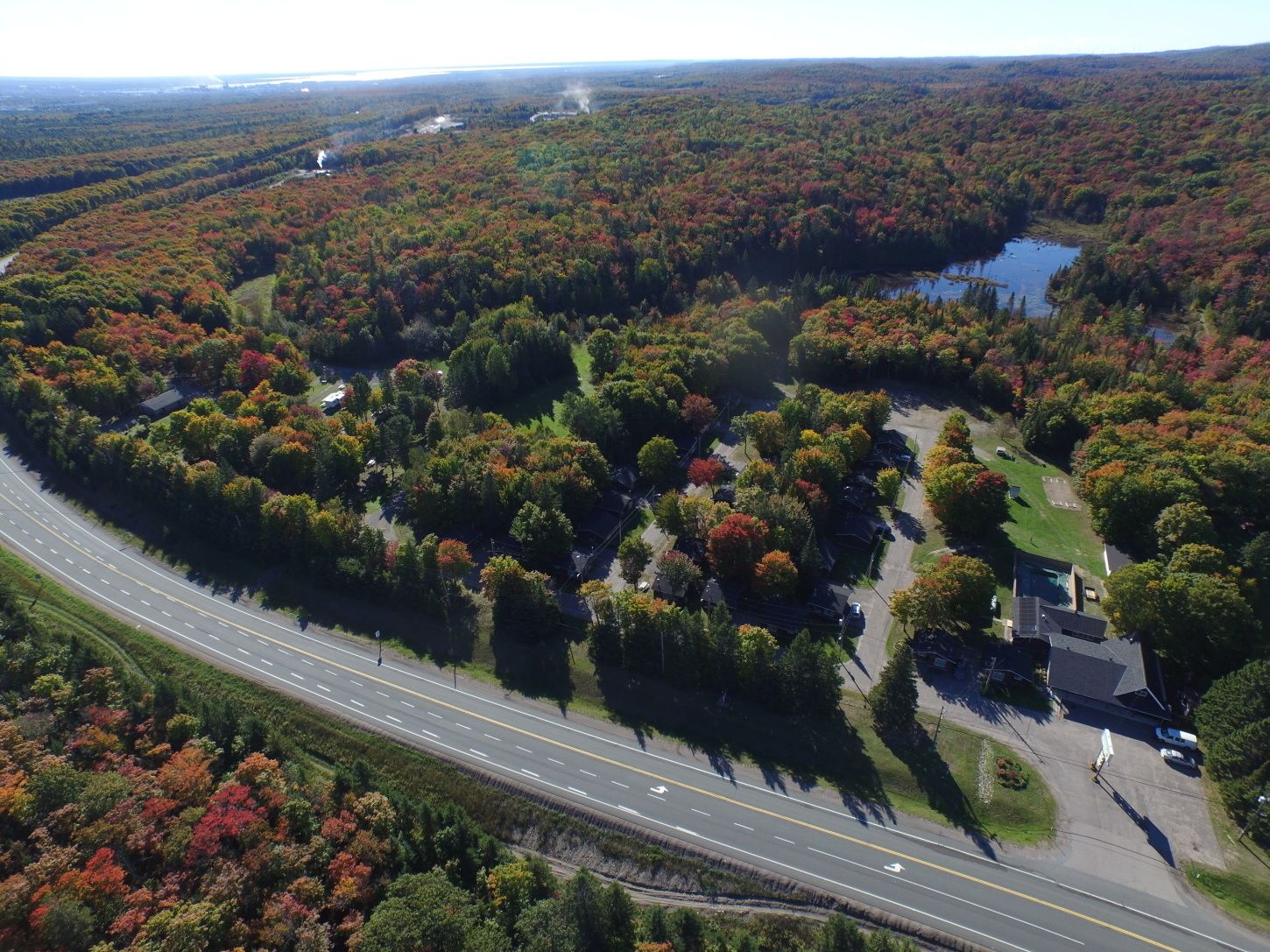 An aerial view of a highway curving through a forested area with a parking lot and a building with a sloped roof.