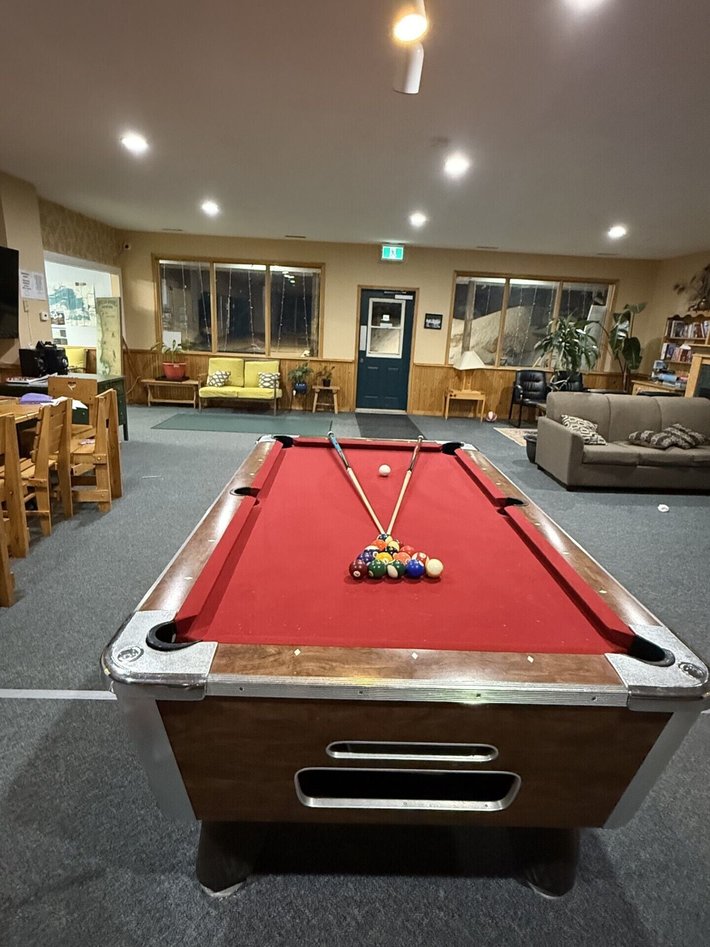 A pool table in a room with a dining area, a sofa, and a door.