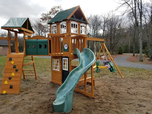 Une structure de jeu en bois comprenant un toboggan, un mur d’escalade et des balançoires.