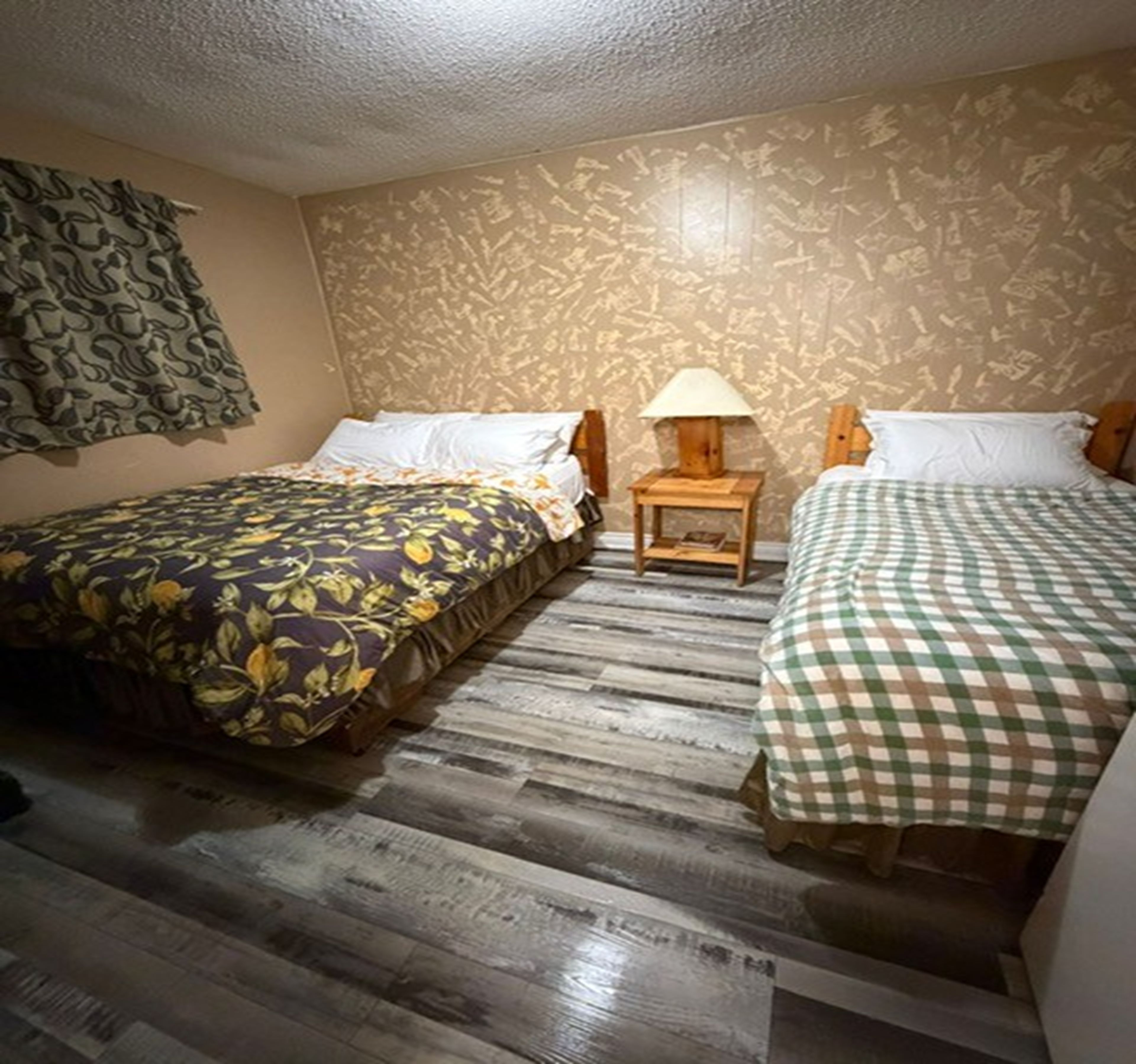 A hotel room with two beds, a small table with a lamp, and patterned wallpaper.