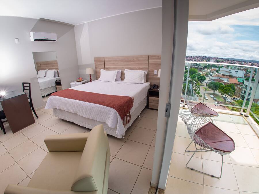 A modern hotel room with a large bed, a balcony with a view of the city, and a seating area with a table.