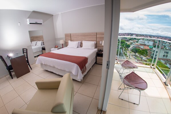 Habitación de hotel moderna con una cama grande, un balcón con vistas a la ciudad y una zona de estar con una mesa.