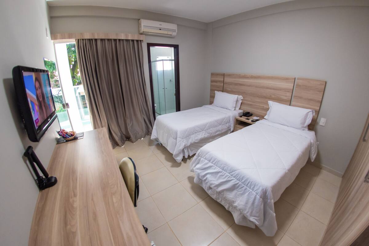 A hotel room with two beds, a desk, a chair, and a television.