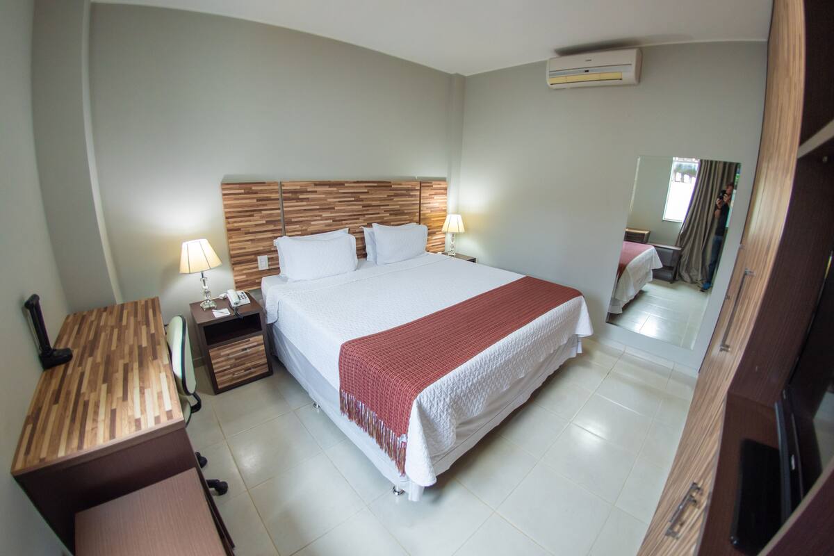 A hotel room with a large bed, bedside tables, a desk, and a mirror.