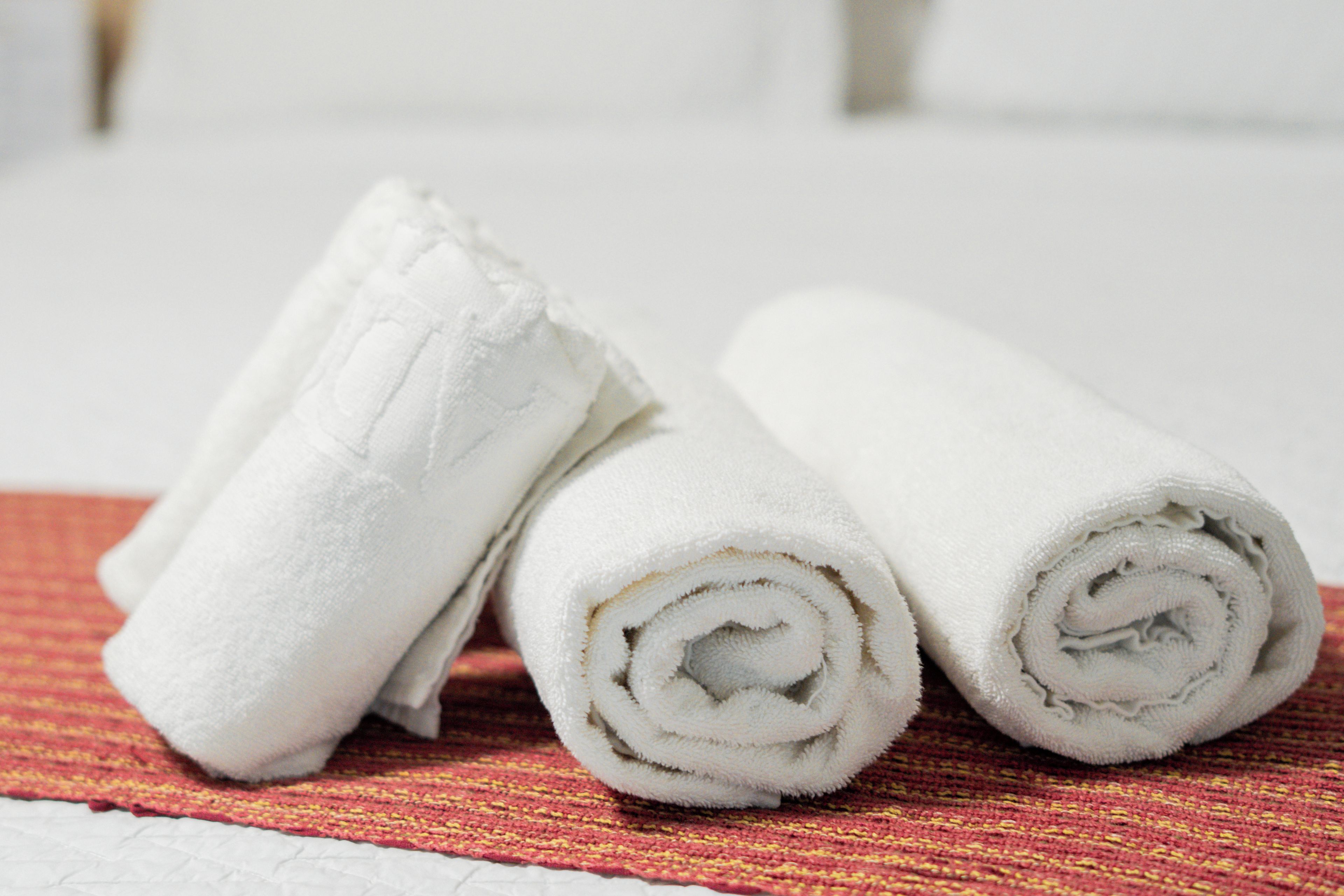Three rolled white towels on a textured red and yellow woven mat.