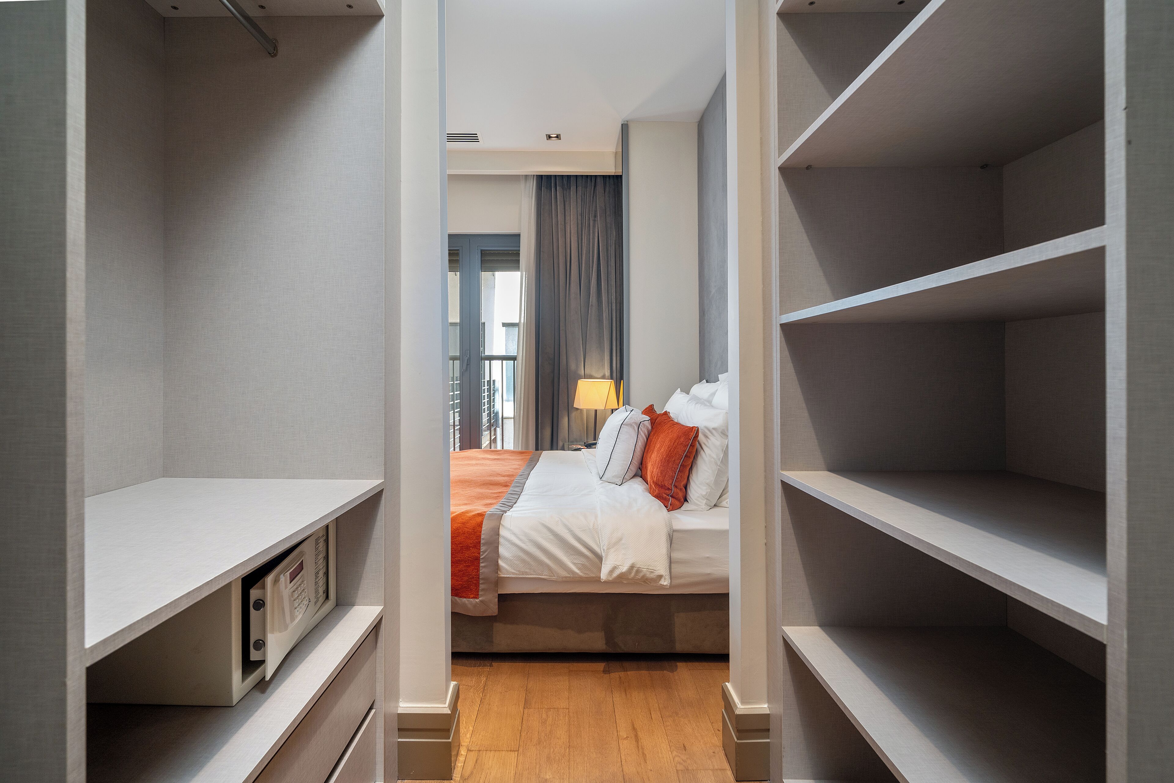 A hotel room with a bed, a nightstand, a lamp, and built-in shelving.