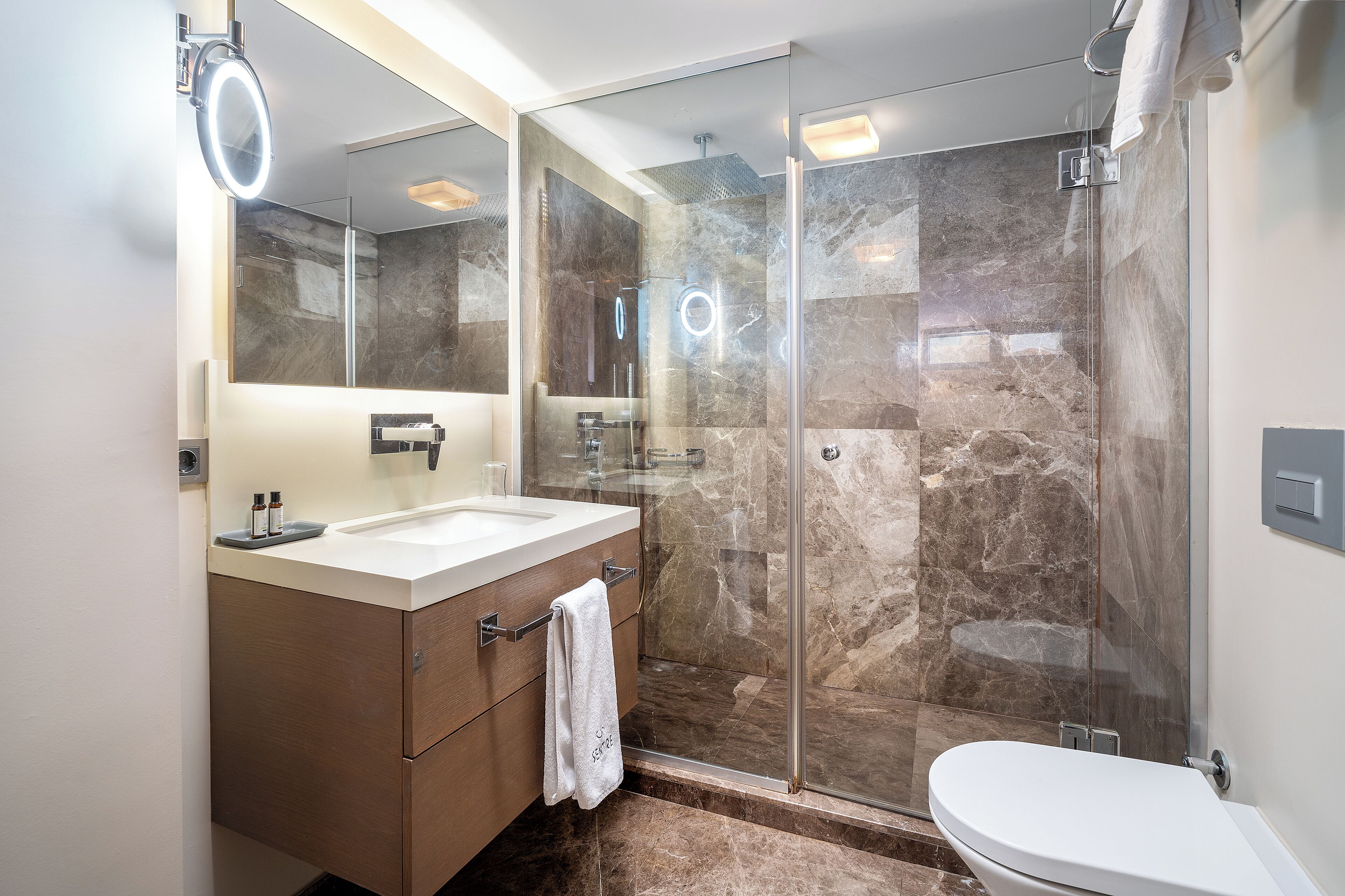 Une salle de bain moderne dotée d’une douche à parois de verre, d’un lavabo blanc et d’un grand miroir avec éclairage intégré.