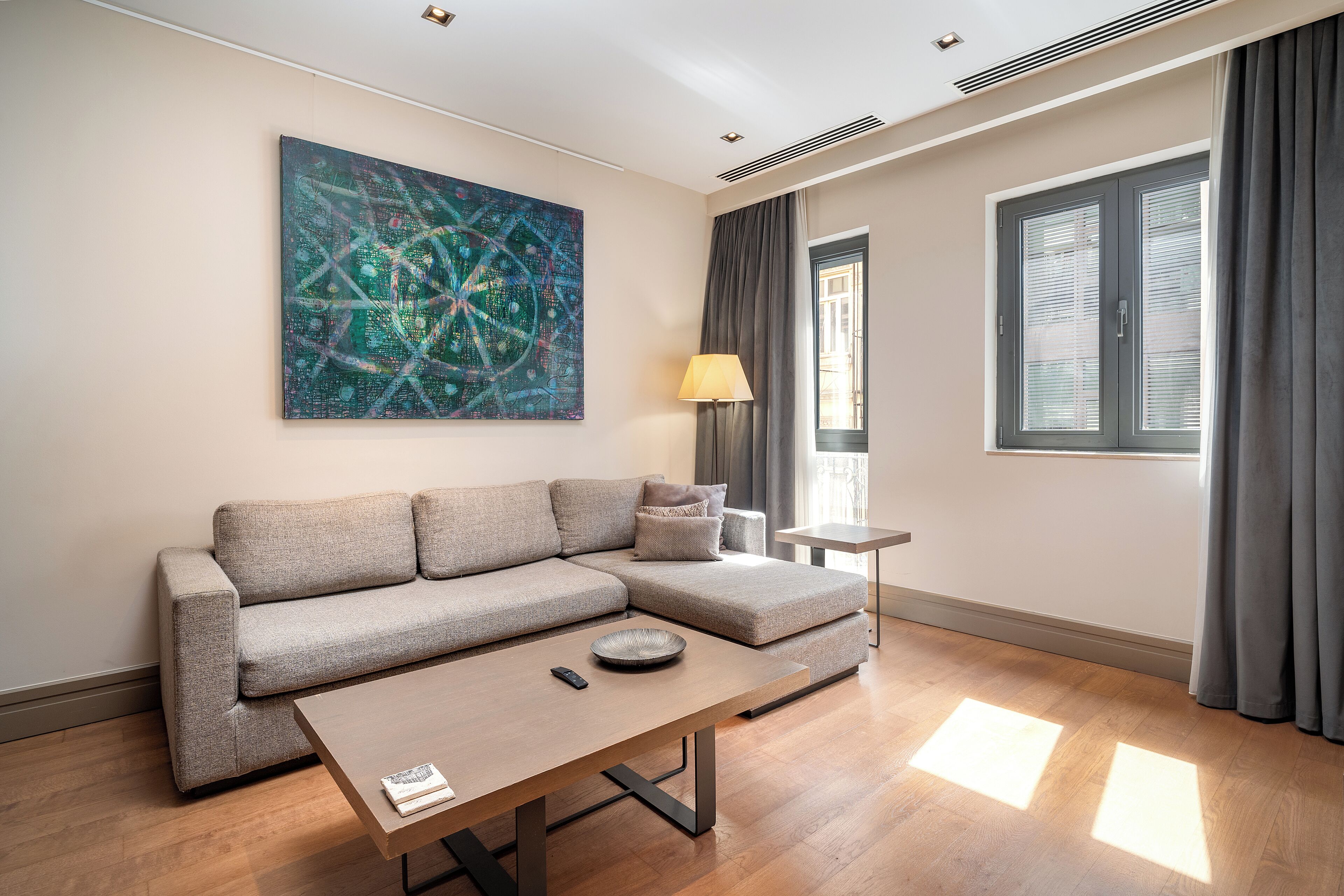 A modern living room with a sectional sofa, a small side table, a lamp, and a large abstract painting on the wall.