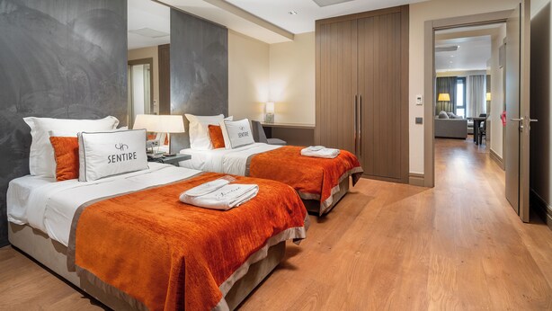 A hotel room with two beds, a large mirror, wooden flooring, and a view into the adjacent room. - Sentire Hotels&Residences Taksim (Istanbul)