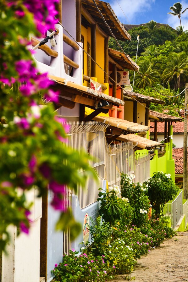 A narrow cobblestone street lined with colorful buildings, a bamboo fence, and lush greenery. - Apartamentos Pipa Centro (Tibau do Sul)