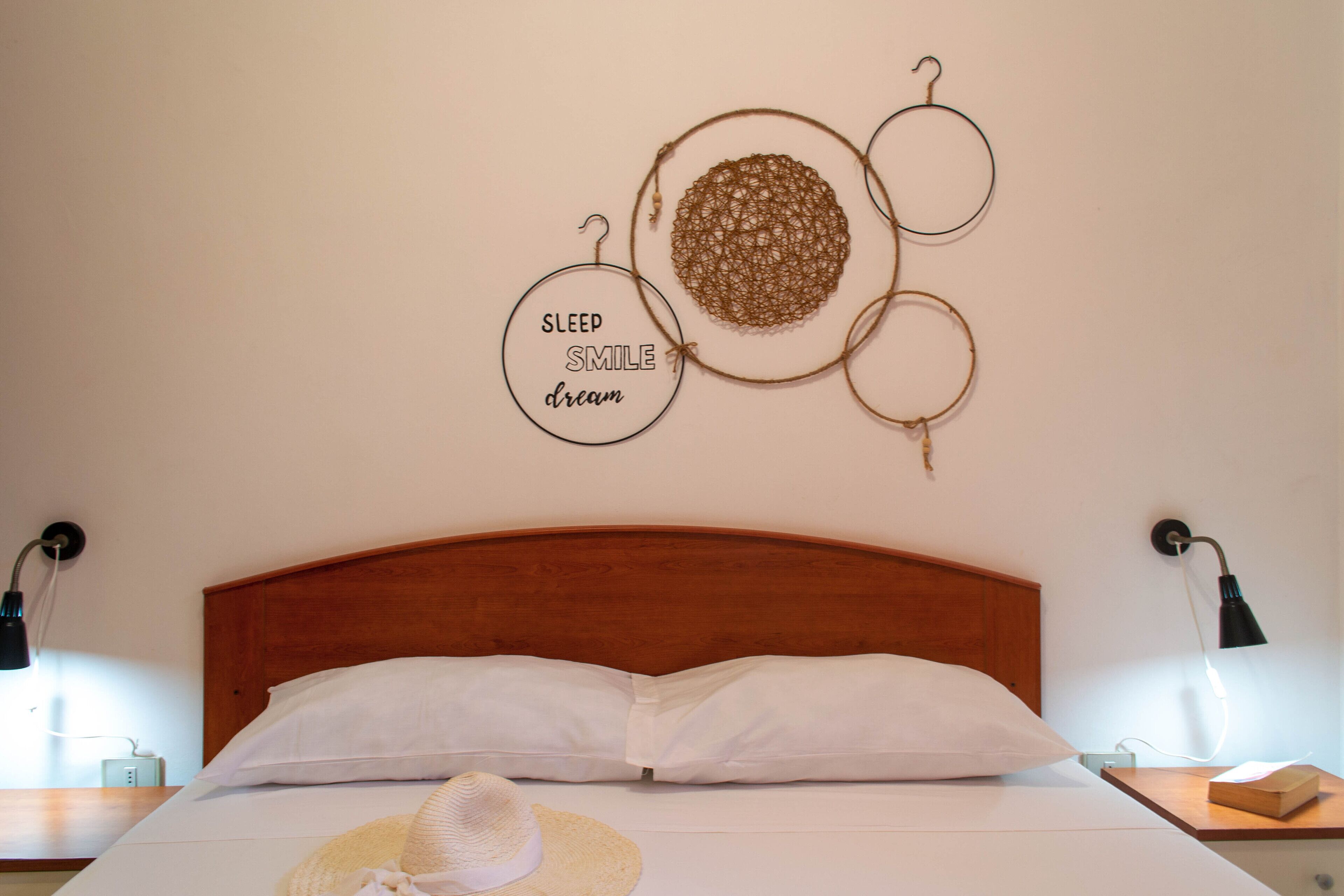 A neatly made bed with white linens and a straw hat on the bed.