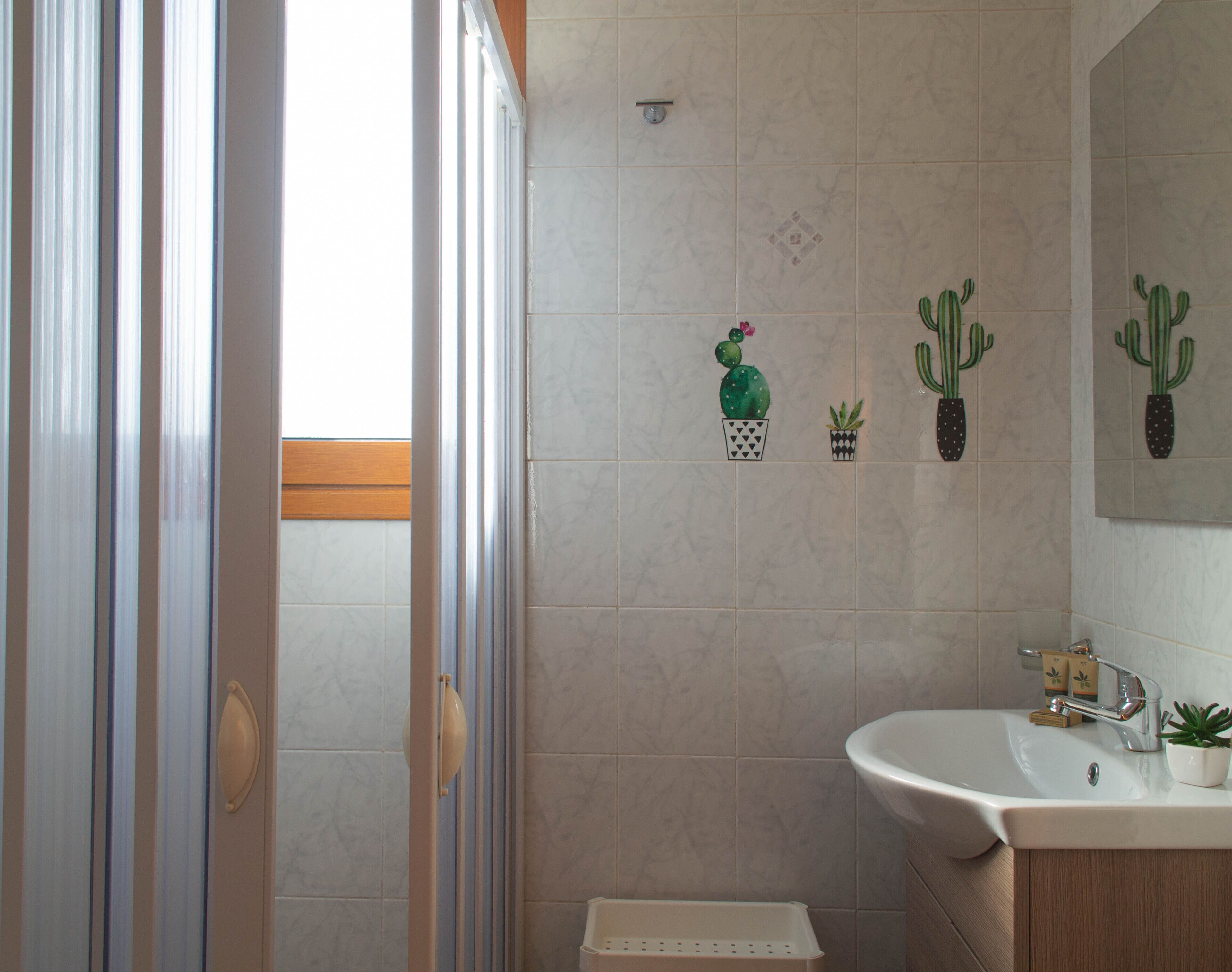 A bathroom with a shower, sink, and decorative cactus wall art.