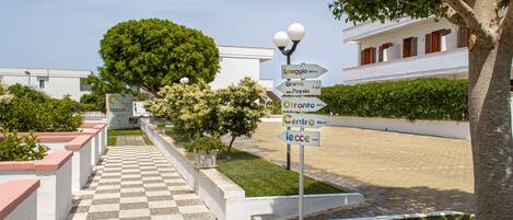 A pathway leading to a building with directional signs, a tree, and a checkered pavement.