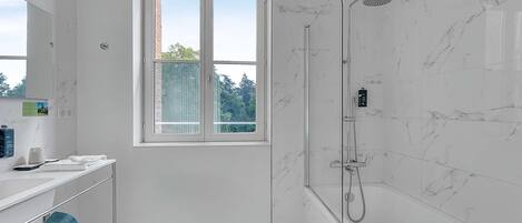 Une salle de bain moderne avec une douche à parois de verre, un meuble-lavabo avec un miroir et une fenêtre donnant sur les arbres.