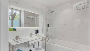 Un baño moderno con ducha de vidrio, lavamanos de mármol blanco y un espejo grande.