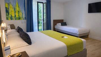 A hotel room with two beds, a large painting, and a view of greenery through the window.