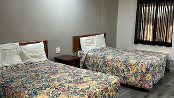 Camera d'albergo con due letti, testiere in legno e una finestra con tende.