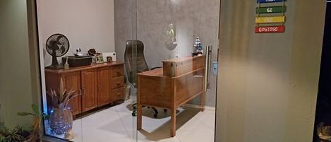 Une pièce avec une cloison en verre, un bureau en bois, une chaise, un ventilateur et un luminaire suspendu.
