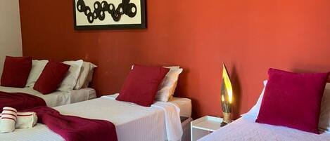 A hotel room with two beds, red and white bedding, an air conditioning unit, a wall-mounted artwork, and a bedside lamp.