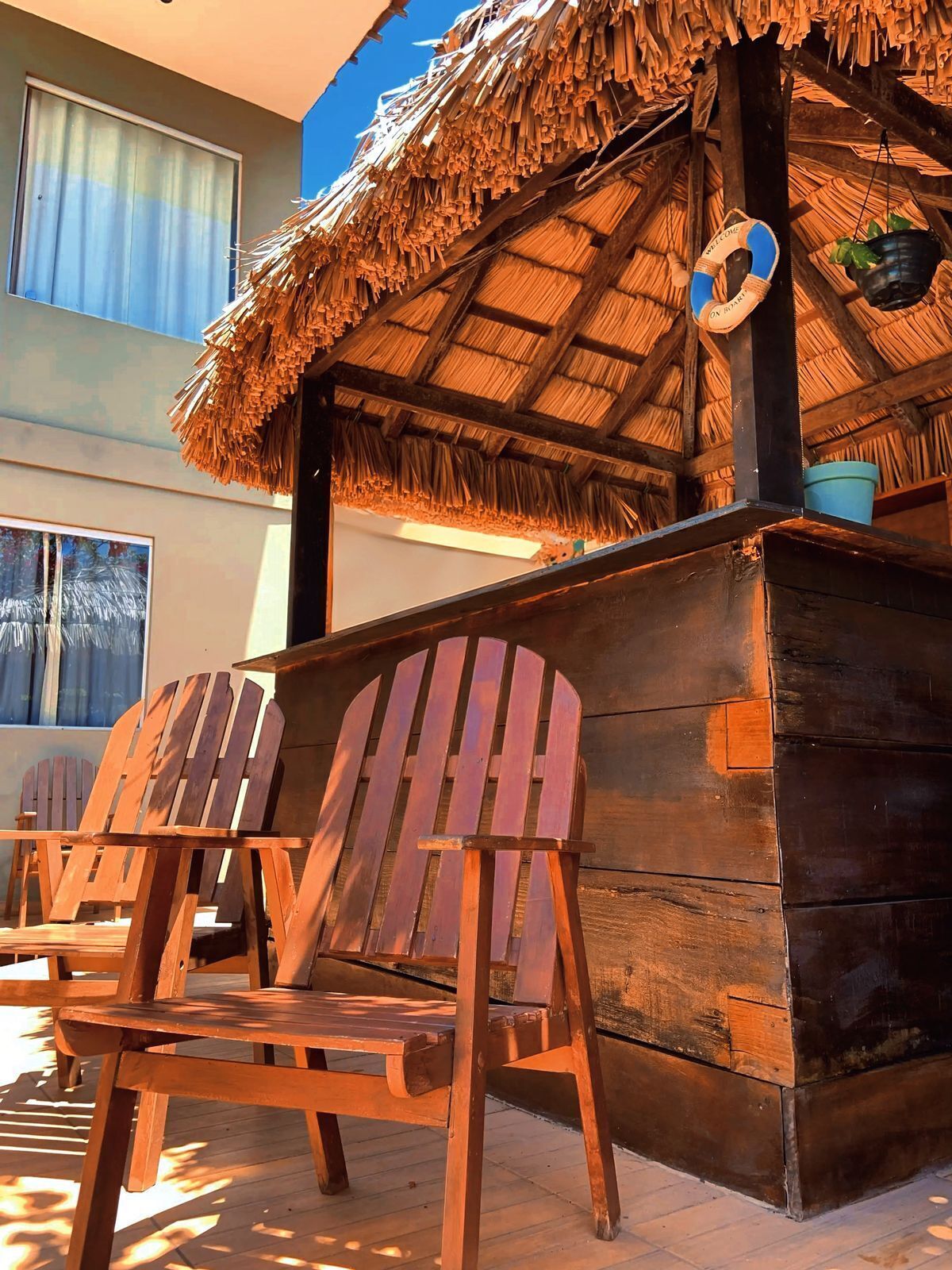 A wooden structure with a thatched roof, wooden chairs, and a blue bucket.