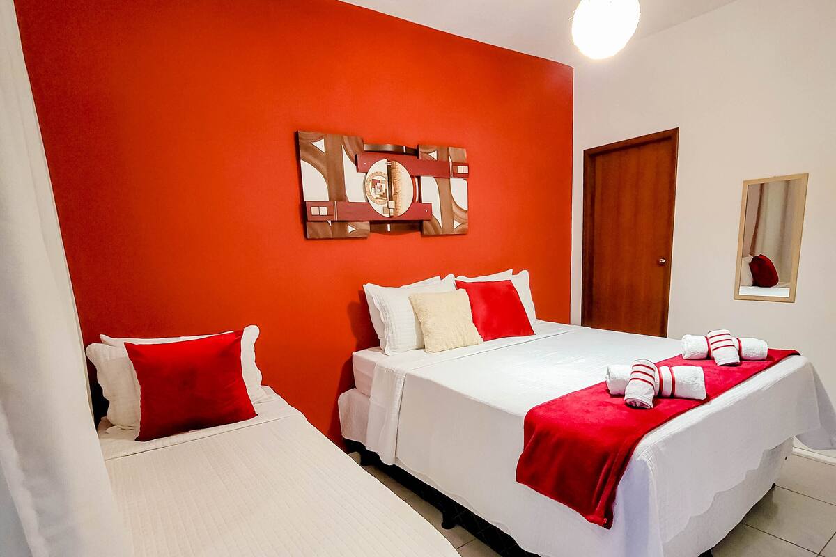 Habitación de hotel con dos camas, ropa de cama roja y blanca, una puerta de madera y una obra de arte colgada en la pared.