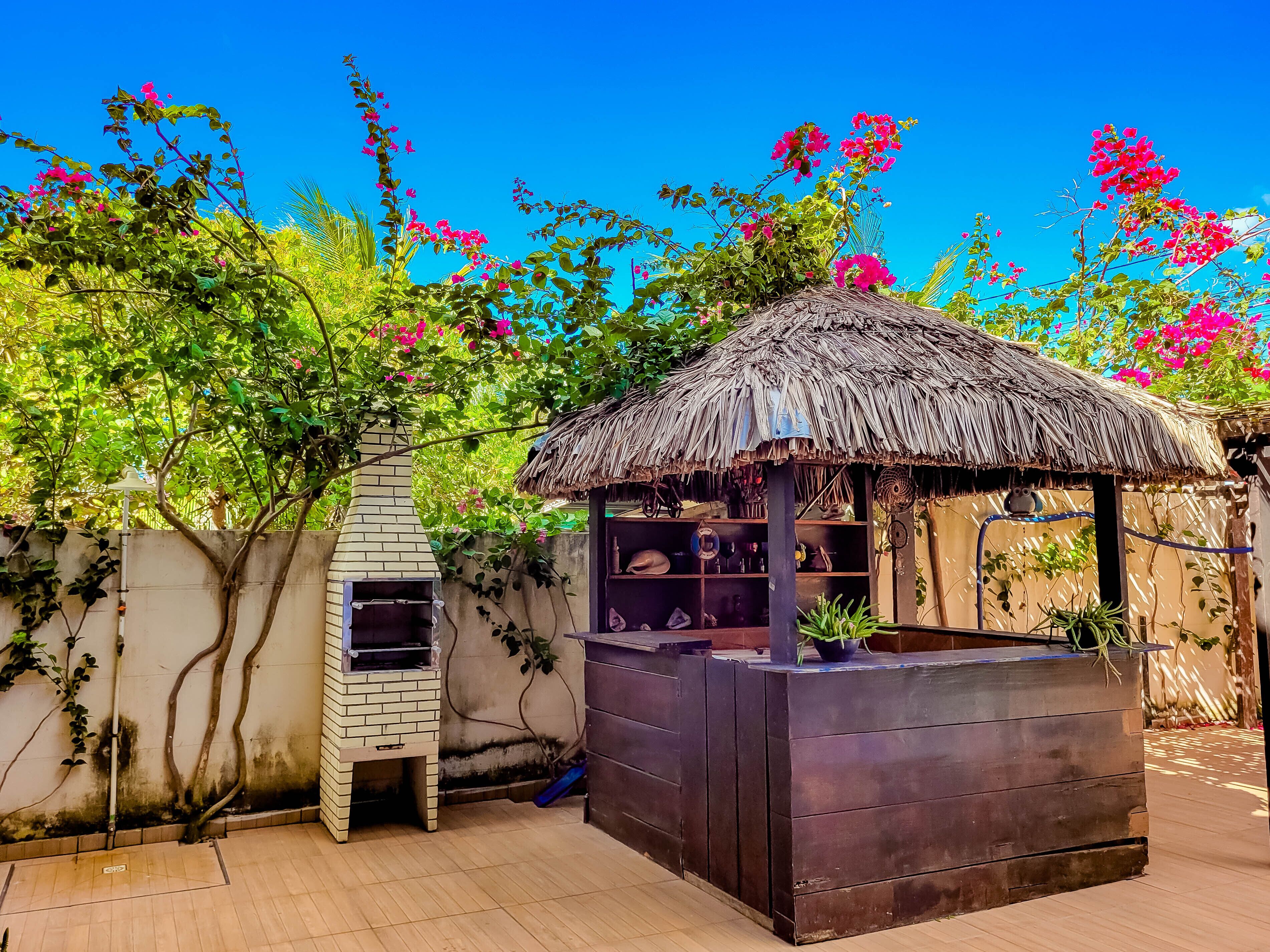 A rustic outdoor area with a brick oven, a wooden structure with shelves, and a thatched roof.