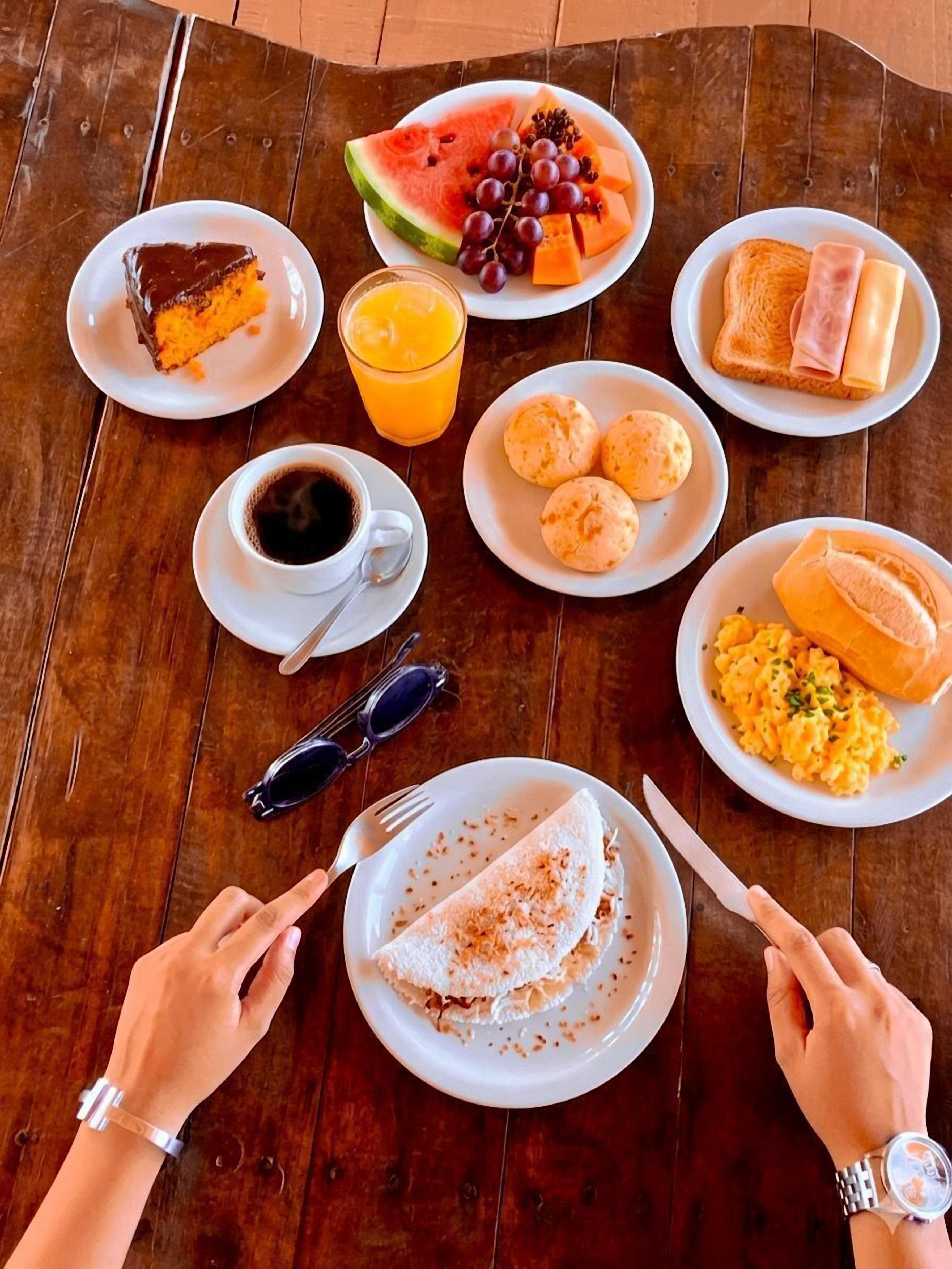 Una mesa de madera con alimentos para el desayuno, como tostadas, jamón, huevos y una porción de pastel.