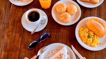 Una mesa de madera con alimentos para el desayuno, como tostadas, jamón, huevos y una porción de pastel.