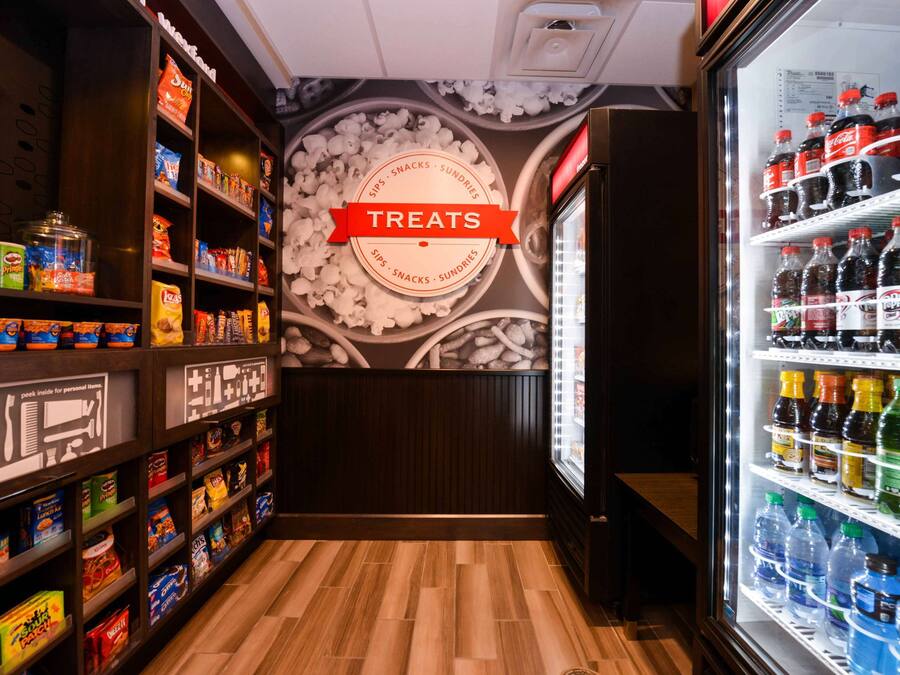 Zona de aperitivos y bebidas con estantes llenos de diferentes opciones y un refrigerador repleto.
