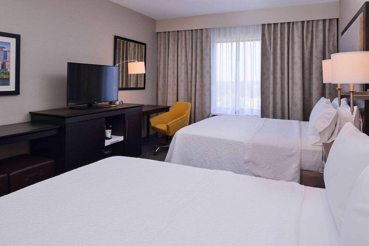 A hotel room with two beds, a desk, a television, and a chair.
