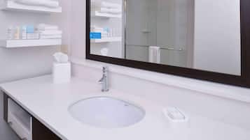 Een moderne badkamer met een grote spiegel, een witte wastafel en planken met handdoeken en toiletartikelen.