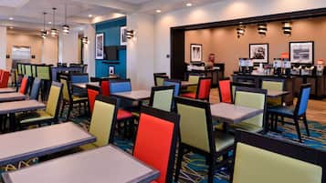 A hotel dining area with multiple tables and chairs, a coffee station, and framed pictures on the walls.